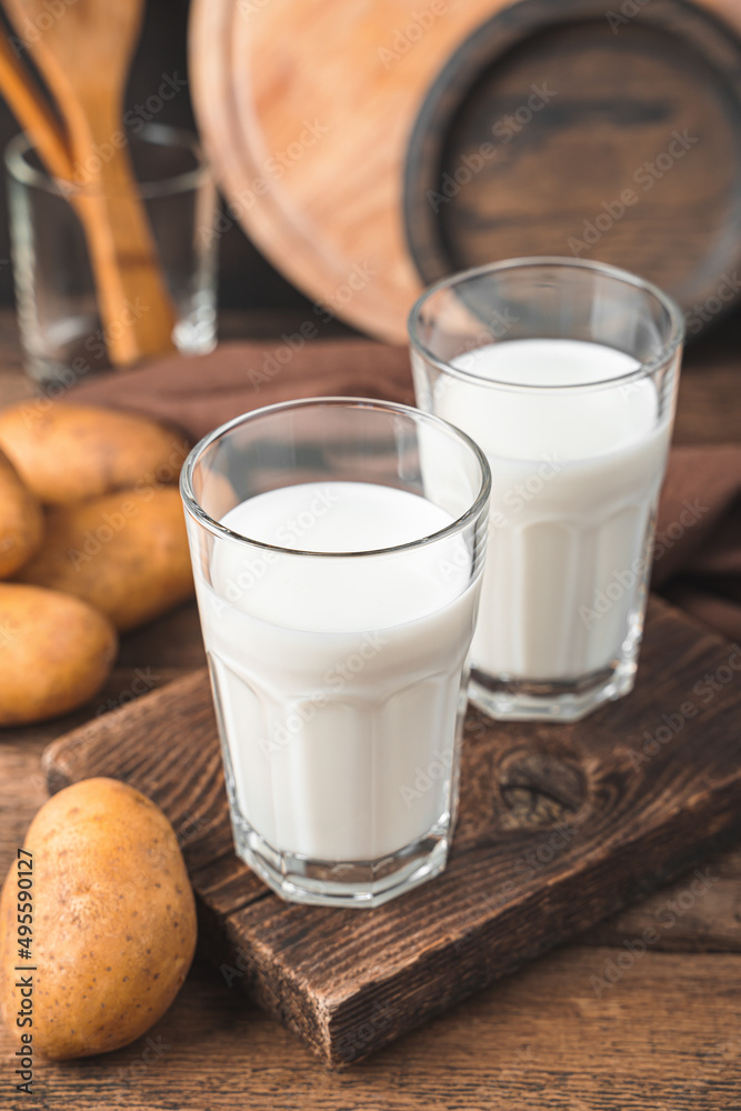 Two glasses of potato milk with raw potatoes on a brown background. Two glasses of potato milk with raw potatoes on a brown background.