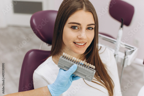 A female dentist helps her patient choose the color of the implant or crown using a color scale