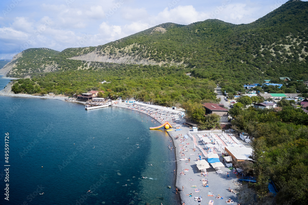The coastline of the resort village in a mountainous area. Beach infrastructure with vacationing tourists. Shooting from a drone.