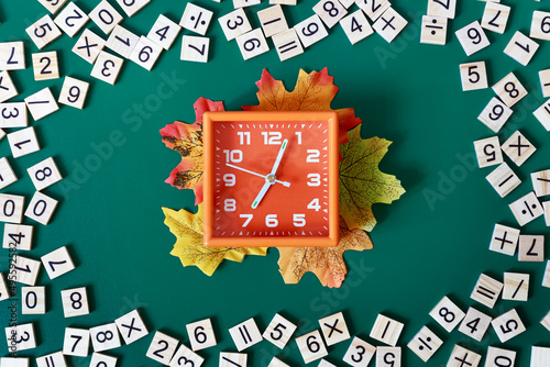Orange alarm clock showing 7 am surrounded by math numbers on green background. Back to school concept. Flat lay.
