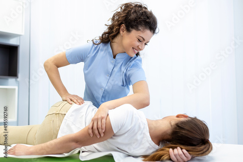 Young doctor chiropractor or osteopath fixing lying womans back with hands movements during visit in manual therapy clinic. Professional chiropractor during work photo
