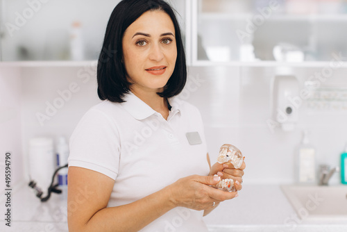 Beautiful female dentist holding a mock up of the jaw in a dental clinic