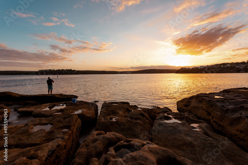 A fisherman on the rocks as the sun sets over the bay