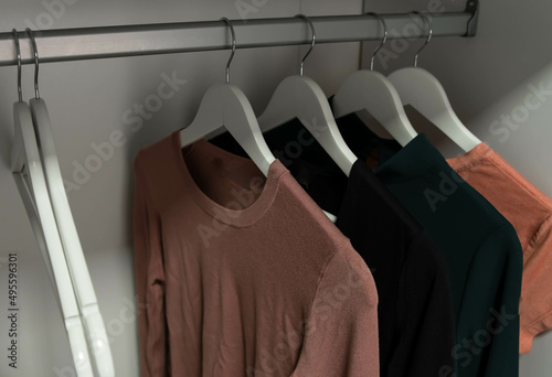 Wooden hangers. Close up of white hangers. Clothes on a rail in a wardrobe. Seasonal capsule for easy dressing, order in things, cleaning out. Clothing hangs on hangers. Order in the closet