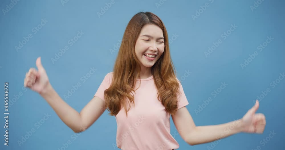 Attractive cheerful youth Asia lady wear casual pink smile show thumps up with positive of content and happy stand isolate over blue background, Satisfaction with quality and recommendation concept. Attractive cheerful youth Asia lady wear casual pink smile show thumps up with positive of content and happy stand isolate over blue background, Satisfaction with quality and recommendation concept.