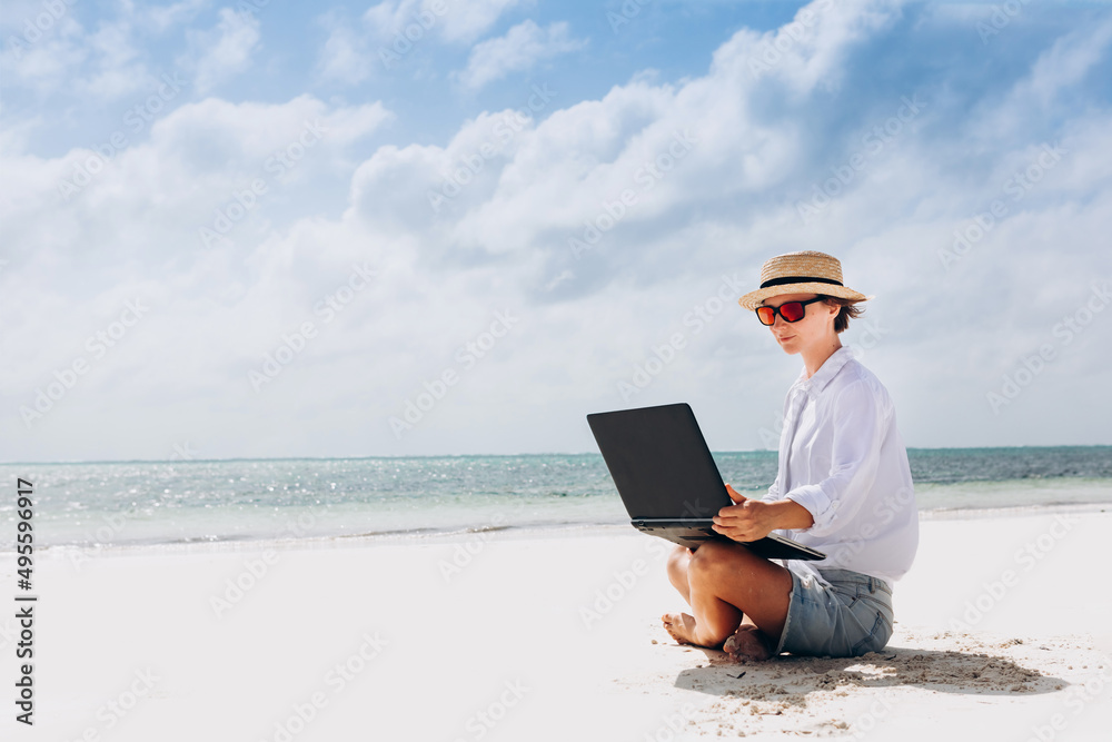 woman using and typing on laptop computer while sitting on the beach