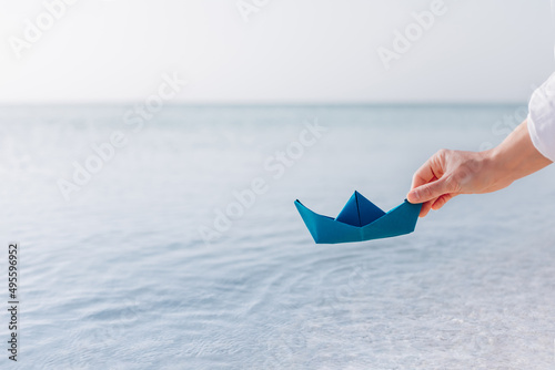 A woman's hand lowers a paper boat into the water