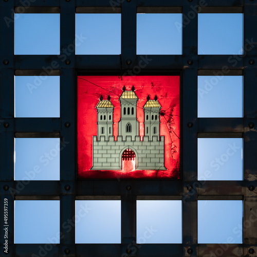 Bratislava city crest symbol, coat of arms in stained glass set in iron grid, backlit against clear blue sky 