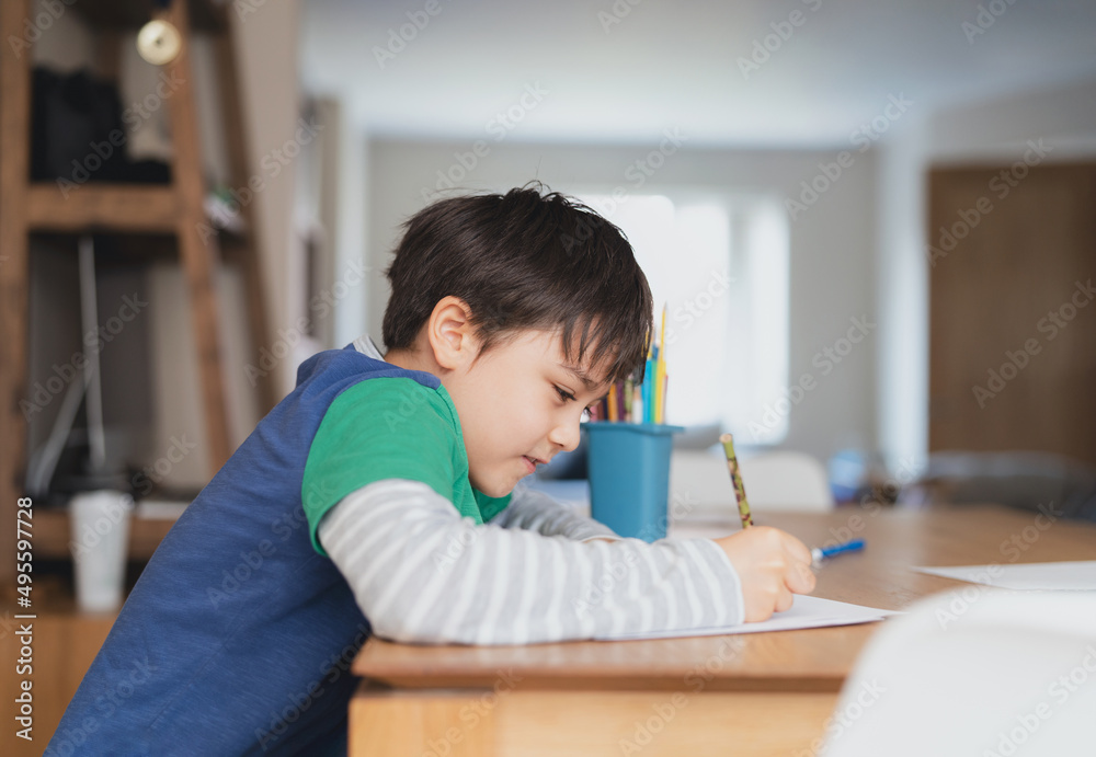 Happy boy using pencil drawing or sketching on paper,Portrait kid siting on table doing homework in living room,Child enjoy art and craft activity at home on weekend,Education, Home schooling concept Happy boy using pencil drawing or sketching on paper,Portrait kid siting on table doing homework in living room,Child enjoy art and craft activity at home on weekend,Education, Home schooling concept