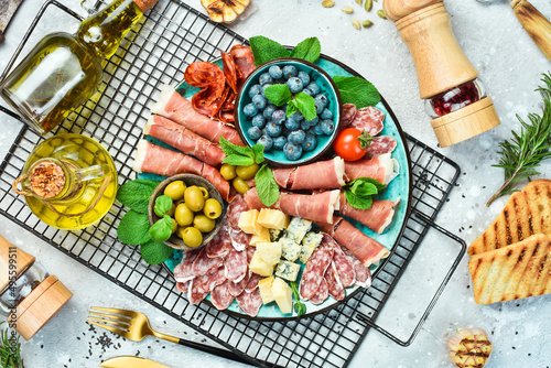 Plate with different kinds of cheese and ham, prosciutto, jamon salami, and snacks. Antipasto Dinner or aperitif party concept. On a gray stone background.