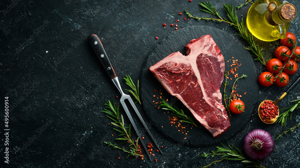 Raw T-bone steak on a stone table with thyme, rosemary and spices. Top view. Flat lay top view on black stone cutting table.