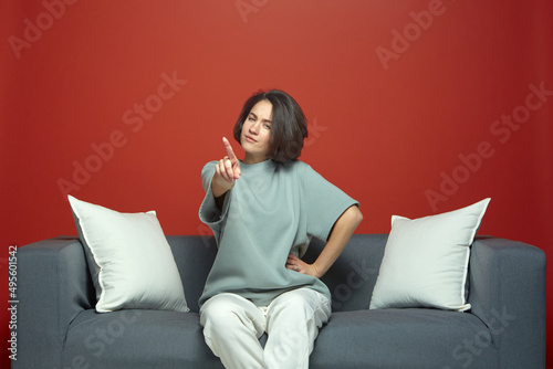 Girl warning, showing admonishing finger gesture, saying no, be careful, scolding, giving advice, sitting on sofa © Georgii
