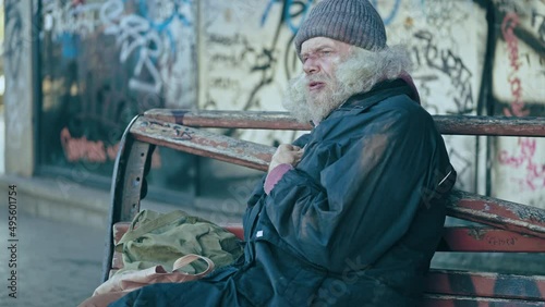 Senior male refugee coughing, suffering flu, sitting alone in deprived district