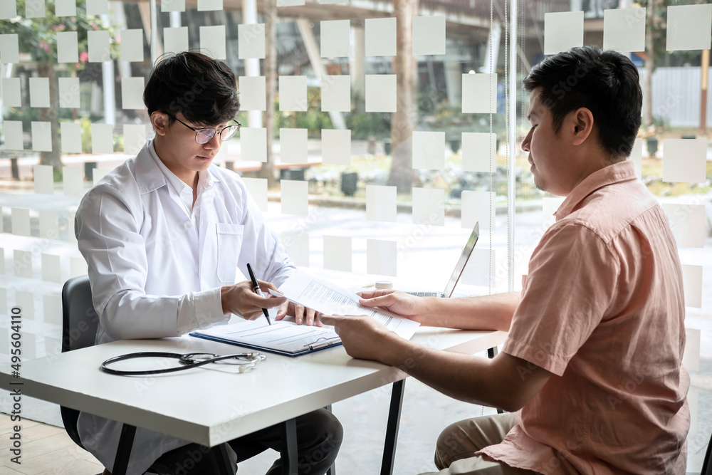 Male doctor discussing with the patient explaining symptoms of the disease after diagnosis checking while recommending treatment methods in clinic Male doctor discussing with the patient explaining symptoms of the disease after diagnosis checking while recommending treatment methods in clinic