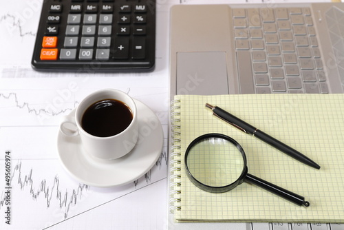 A cup of coffee on the desk among the items and accessories for analyzing and making deals on the stock market. The concepts of business, finance, investment. 