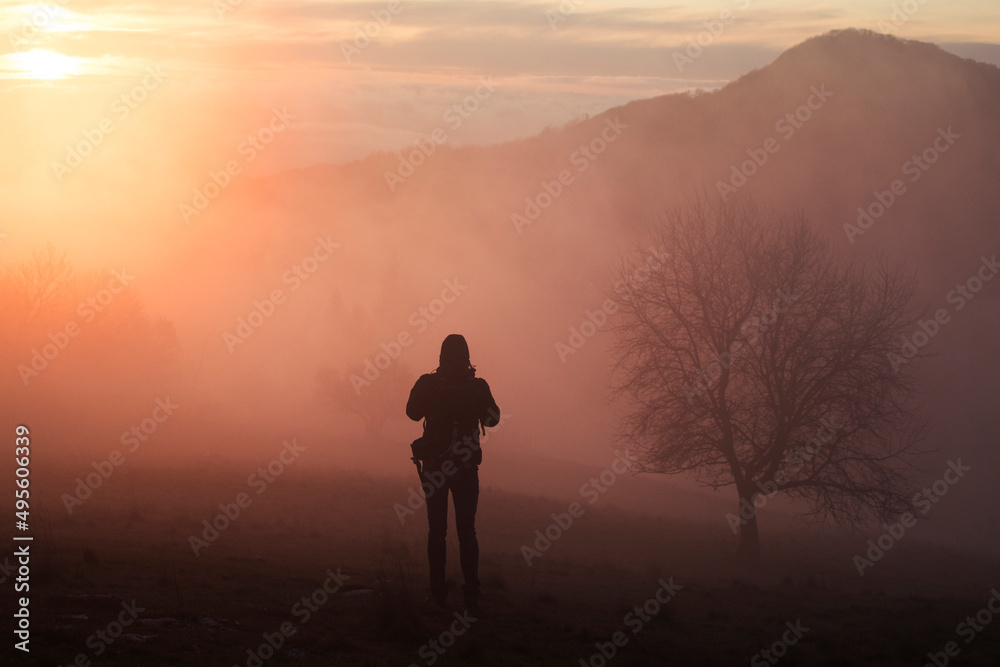 silhouette of a person standing on a mountain at sunset