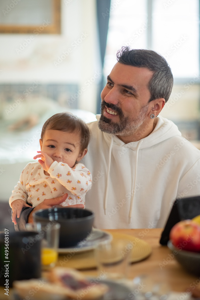 Portrait of happy father sitting at table with baby son. Mid adult man having breakfast in morning with his baby. Fatherhood concept Portrait of happy father sitting at table with baby son. Mid adult man having breakfast in morning with his baby. Fatherhood concept