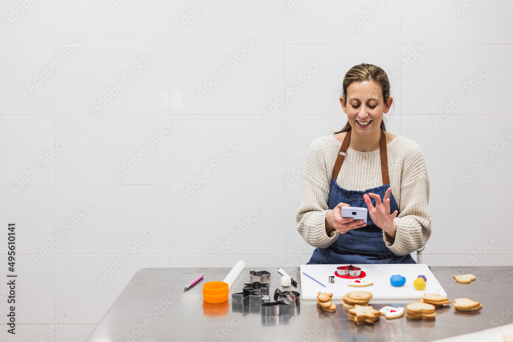 Pastry chef using her phone while decorating cookies in pastry shop Pastry chef using her phone while decorating cookies in pastry shop