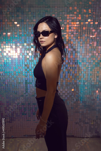 sexy young energetic woman in black clothes and sunglasses in the studio against background of shiny squares © saulich84