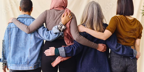 International Women's Day rear view portrait of four women standing with arms around each other in solidarity