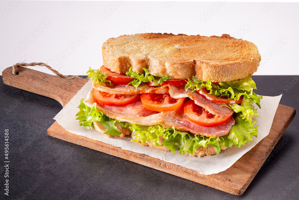 Fresh homemade BLT sandwich with double bacon, lettuce and tomato between toasted doorstep bread slices on wooden board. Fresh homemade BLT sandwich with double bacon, lettuce and tomato between toasted doorstep bread slices on wooden board.