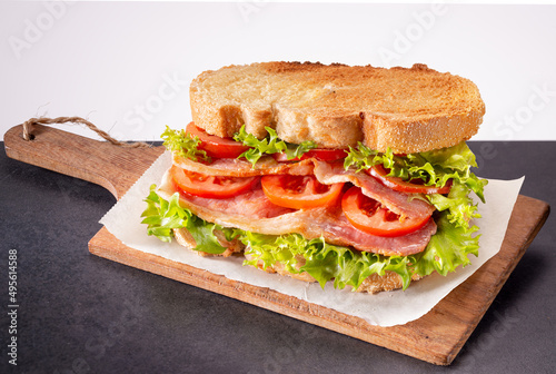 Fresh homemade BLT sandwich with double bacon, lettuce and tomato between toasted doorstep bread slices on wooden board.
