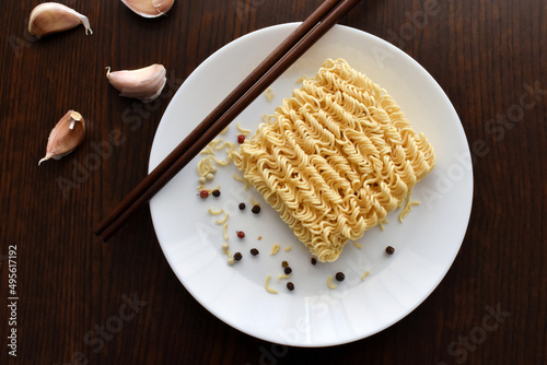 Uncooked instant noodles with peppercorns and chopsticks on a plate. Garlic cloves are beside the plate. Copy space is on the left side. Flat lay top view photo. Food from above concept.