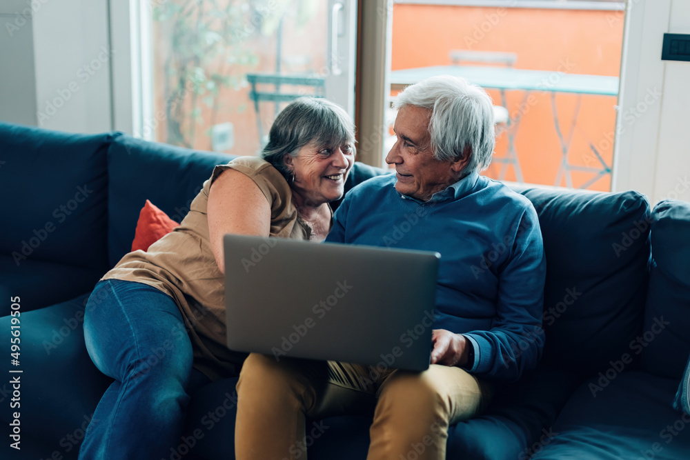 elderly couple sitting on sofa using laptop - smiling seniors