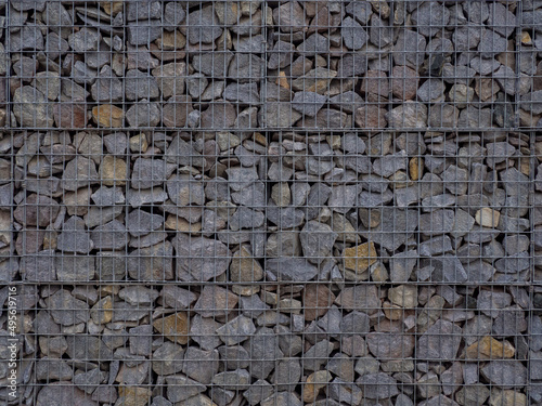 Decorative fence of bulk stone in the grid. Textured background of a stone wall with iron netting. Stone wall in wire frame. Gabion filled with limestone photo