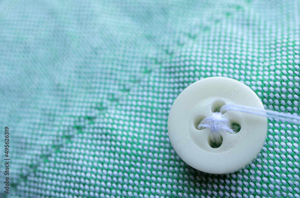 Close up of white sewing button on a green shirt. empty space for text. Craft, needlework concept. Close up of white sewing button on a green shirt. empty space for text. Craft, needlework concept.