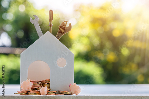 Home models, gold coins, piggy bank, construction equipment and spanners put on the wooden table. Financial planning to build or renovate a home, real estate loan concept.