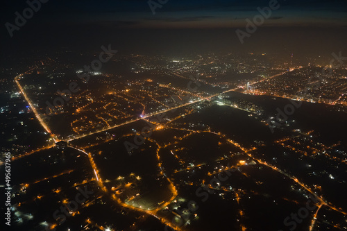 Aerial view from airplane window of buildings and bright illuminated streets in city residential area at night. Dark urban landscape at high altitude