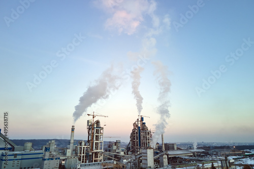 Aerial view of cement plant production area with high concrete factory structure and tower cranes at industrial site. Greenhouse gas smoke polluting air. Manufacture and global industry concept