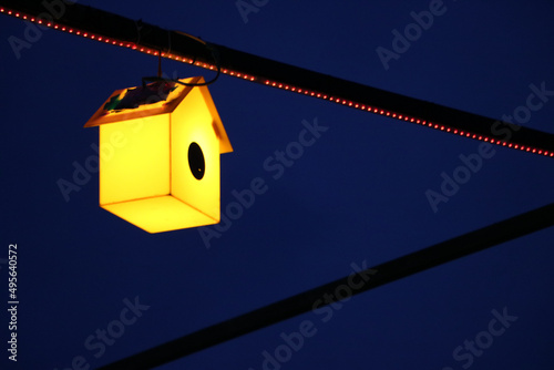 Decorative illuminated yellow birdhouse hanging from a pole Fototapeta