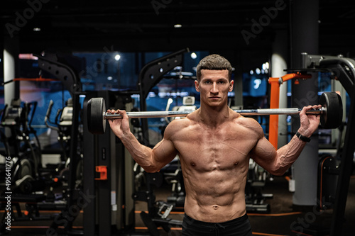 Shirtless strong man lifting barbell in gym, weightlifter