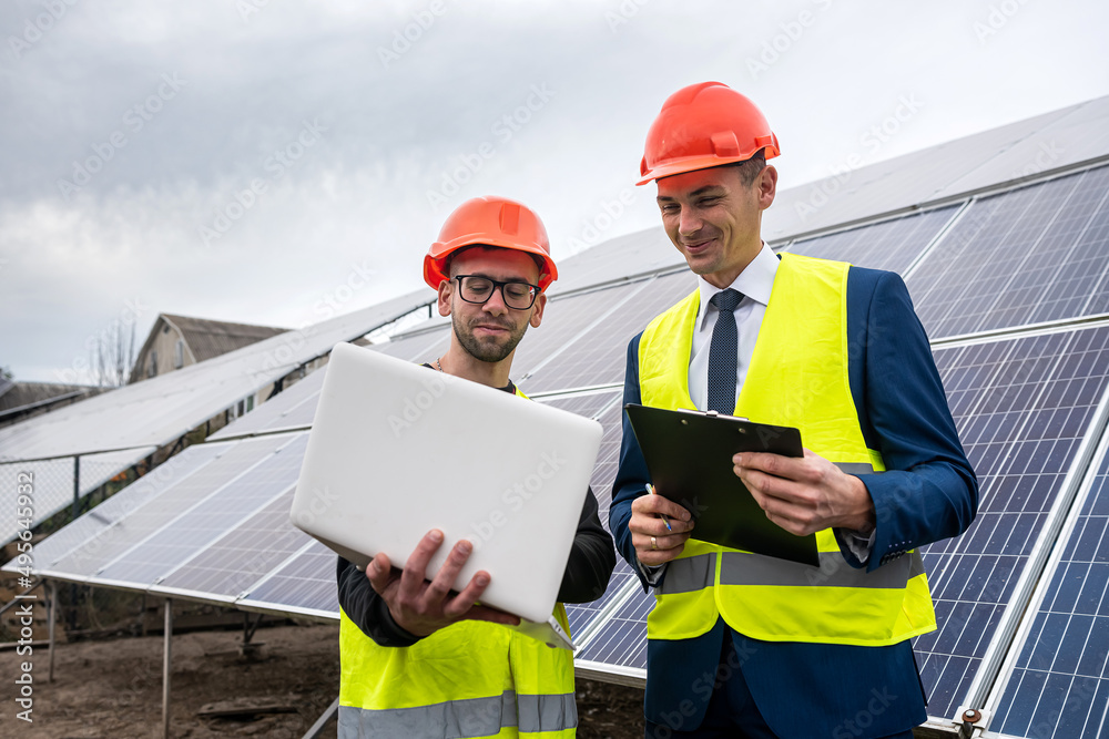 handsome young guys in hard hats with documents stand near the newly installed panels. handsome young guys in hard hats with documents stand near the newly installed panels.