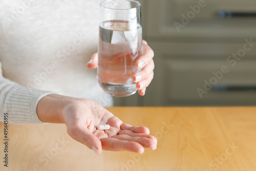 Closeup shot of an unrecognisable woman holding a glass of water and medication in the kitchen.