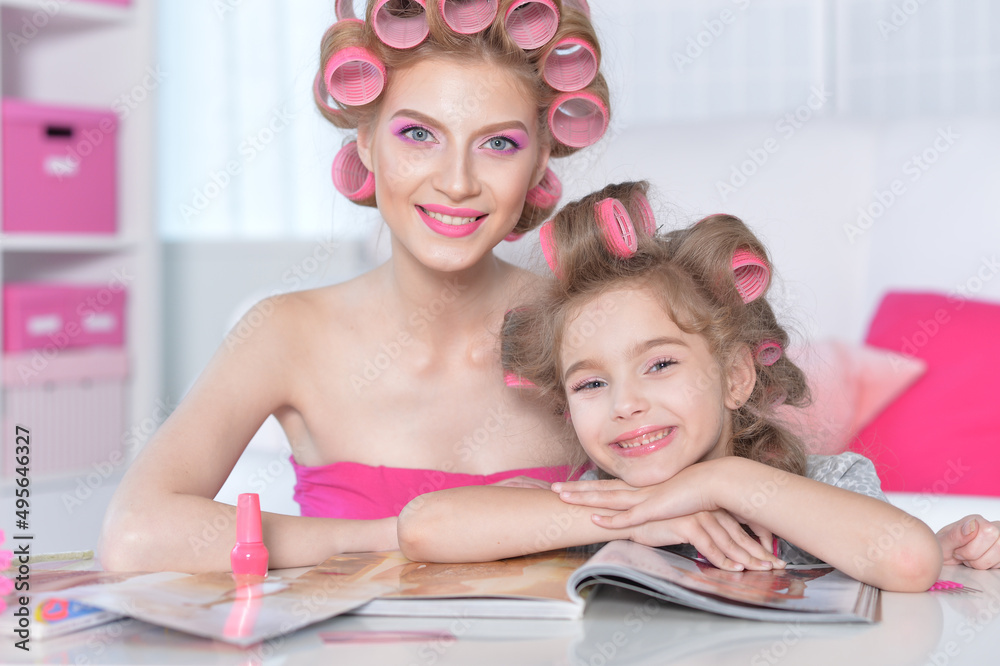 Mother and little daughter with hair curlers reading magazine Mother and little daughter with hair curlers reading magazine