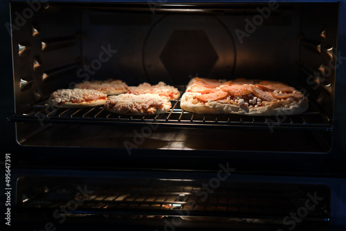 Frozen pizza semi-finished product with tomato sause and cheese on grill prepared for baking in oven. Selective focus
