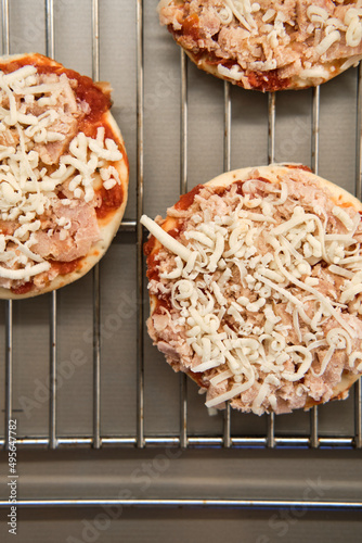 Small frozen pizza semi-finished product with tomato sause and cheese on grill prepared for baking. High angle view.