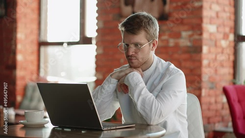 pensive man is reading news in internet and thinking, using laptop in cafe during coffee break, doomsurfing photo