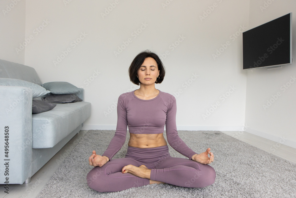 Yoga woman in fitness Wear Doing Exercise at home, sitting on carpet, copy space, full length shot. Healthy, sporty lifestyle, yoga practicing at home