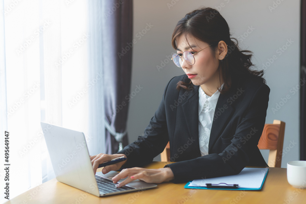 South East Asian businesswoman in Thailand wearing a black suit and typing on a laptop in her office desk. South East Asian businesswoman in Thailand wearing a black suit and typing on a laptop in her office desk.