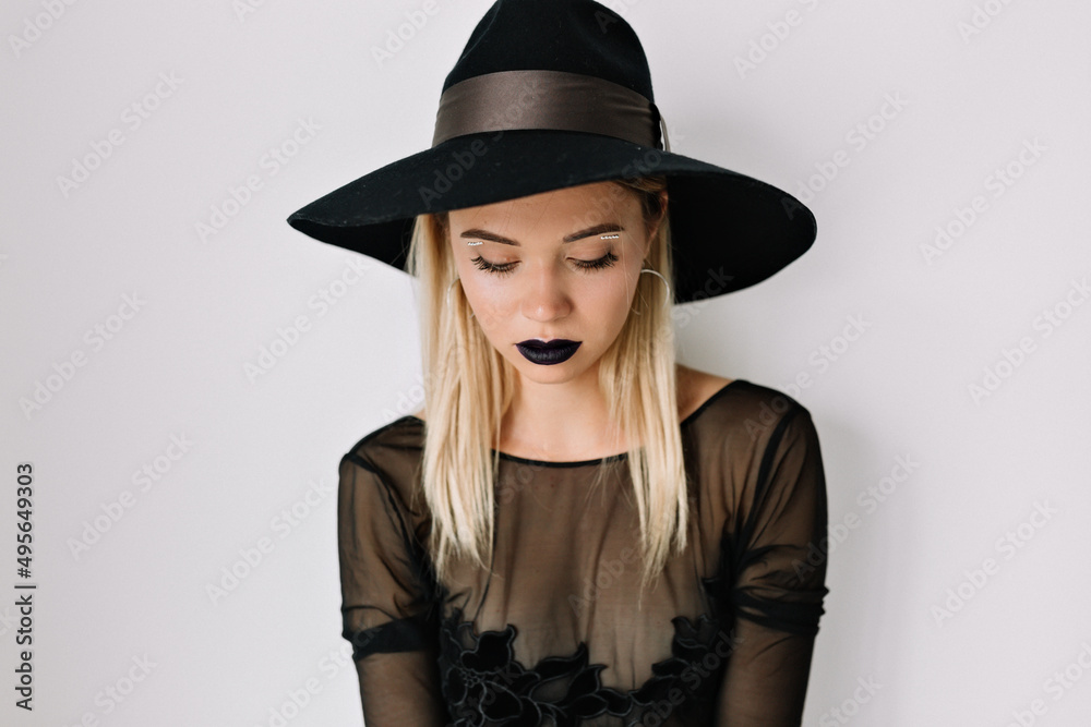 Studio close up portrait of pretty woman with dark lips is wearing hat and blouse is looking down over isolated background Studio close up portrait of pretty woman with dark lips is wearing hat and blouse is looking down over isolated background