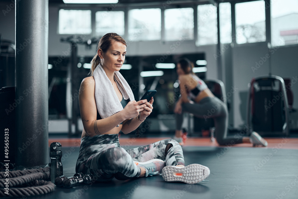 Pretty woman working out in a gym, making pause and using smartphone. Adult pretty sporty lady with beautiful shaped body. Pretty woman working out in a gym, making pause and using smartphone. Adult pretty sporty lady with beautiful shaped body.