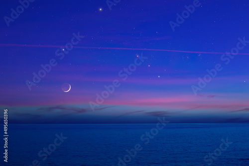 Moon with starry skies and planets above ocean horizon.