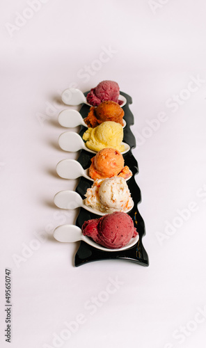 Portrait of a row of different flavored gelatos in different spoons on a white background photo