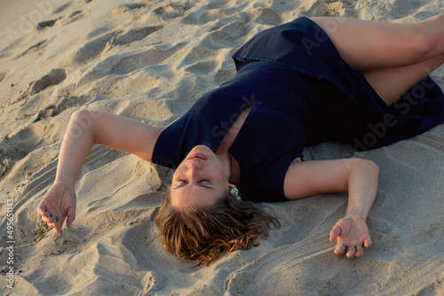 Beautiful woman in a black dress lies on the sand near the sea at sunset