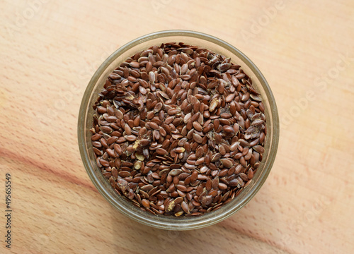 Flax seeds affected by pests. Glass plate with flax seeds on a wooden surface. Dietary fibers of flaxseed.