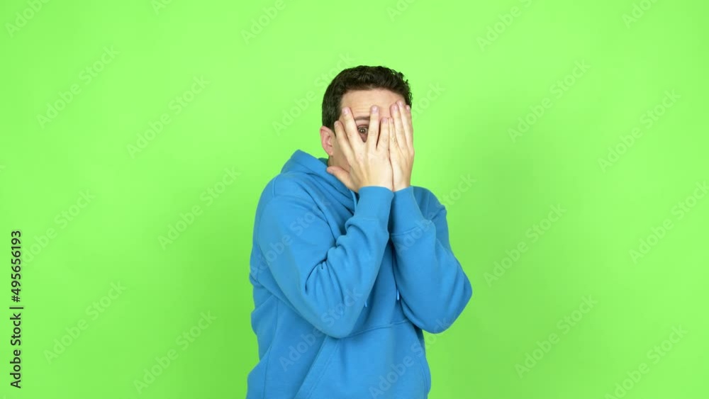 Man covering eyes by hands and looking through the fingers over isolated background. Green screen chroma key Man covering eyes by hands and looking through the fingers over isolated background. Green screen chroma key
